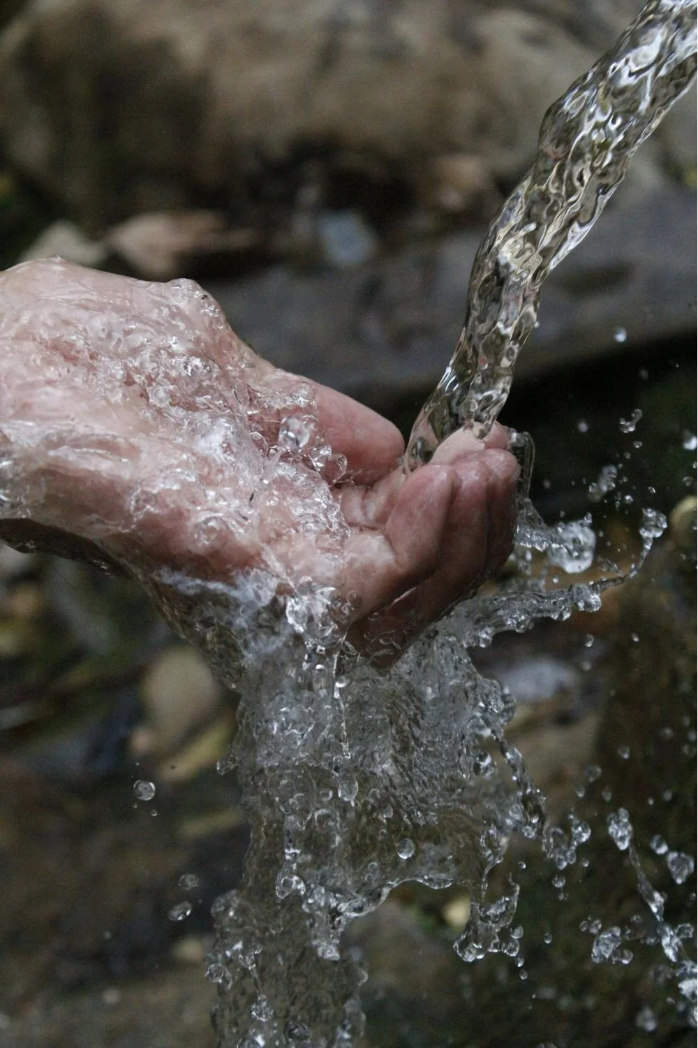 Close-up of hands washing with water from a stream or small waterfall outdoors.