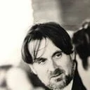 A black and white photo of a man with dark hair and a beard, looking at the camera.