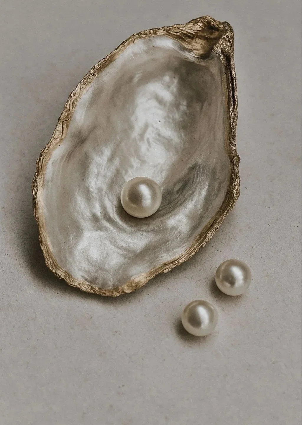 Close-up of an open oyster shell with three pearls inside and two pearls outside on a light surface.