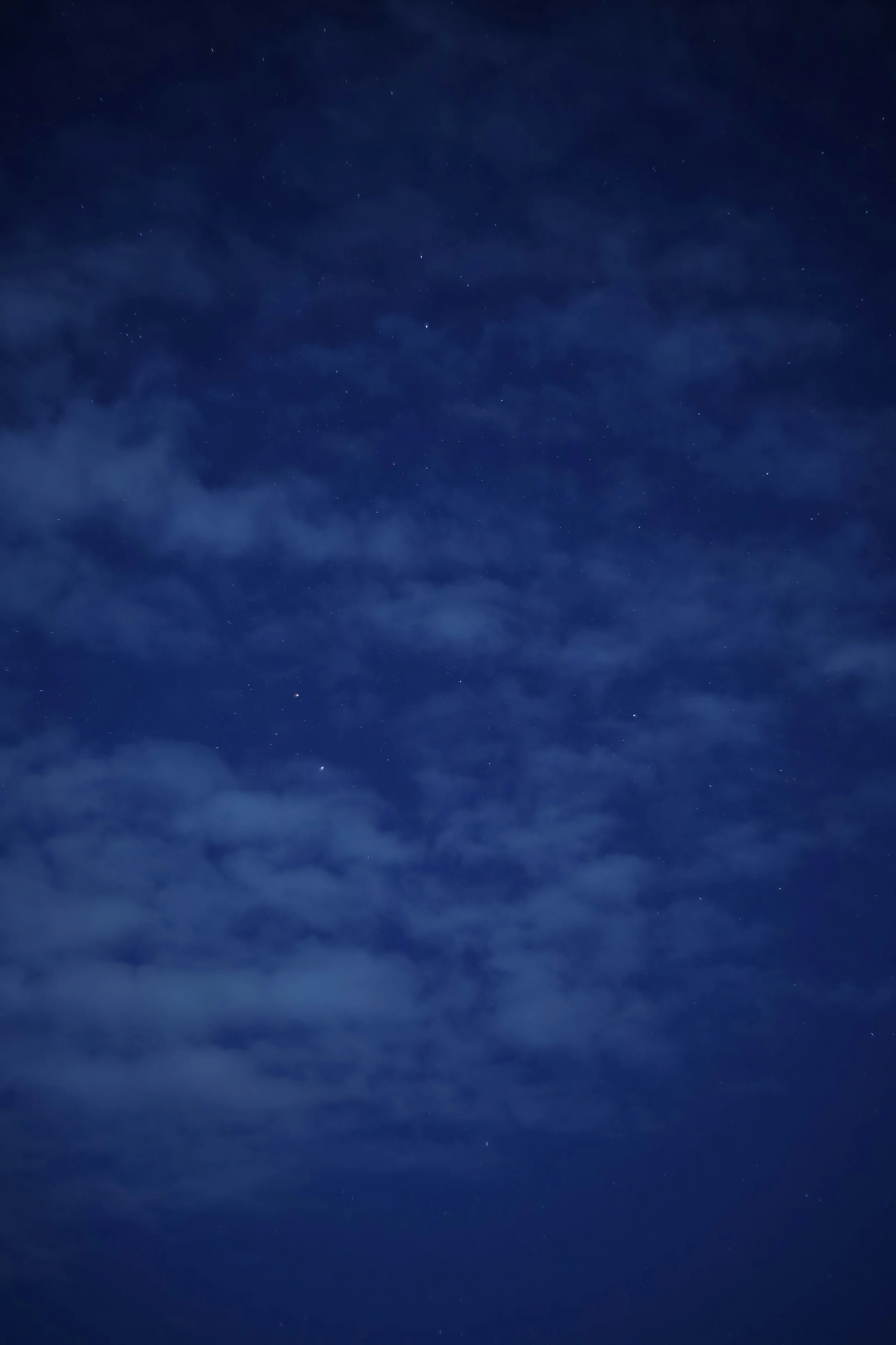 Night sky with stars visible through some clouds.
