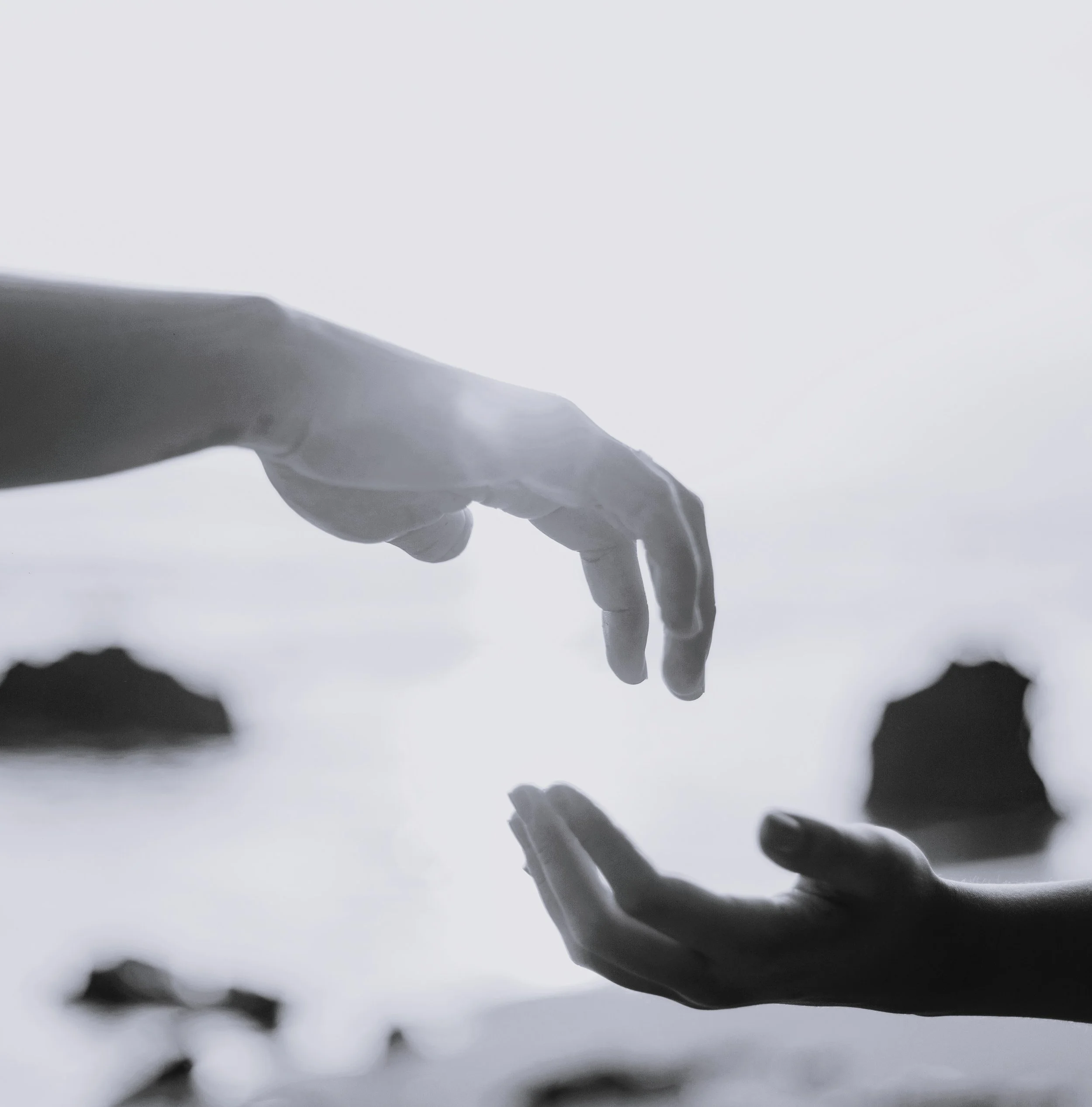 Close-up view of a person's hand and fingers with some water droplets, against a blurred background of water and sky.