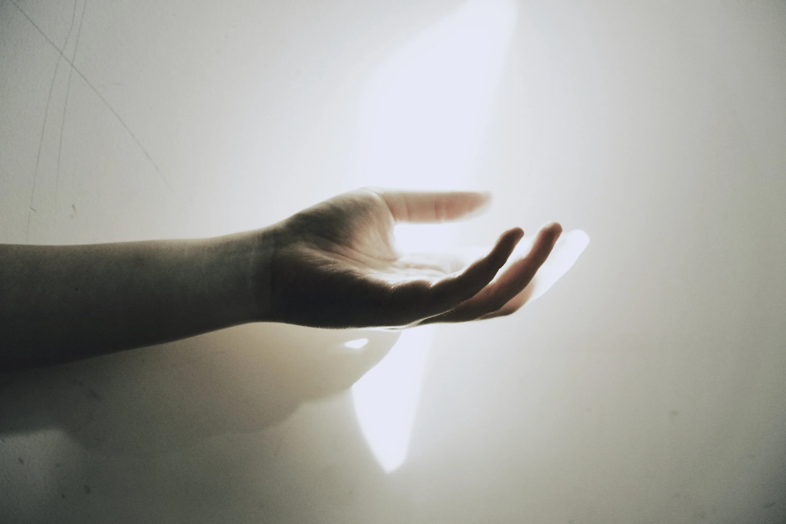 A person's hand with fingers slightly spread, reaching toward a bright beam of light coming from above.