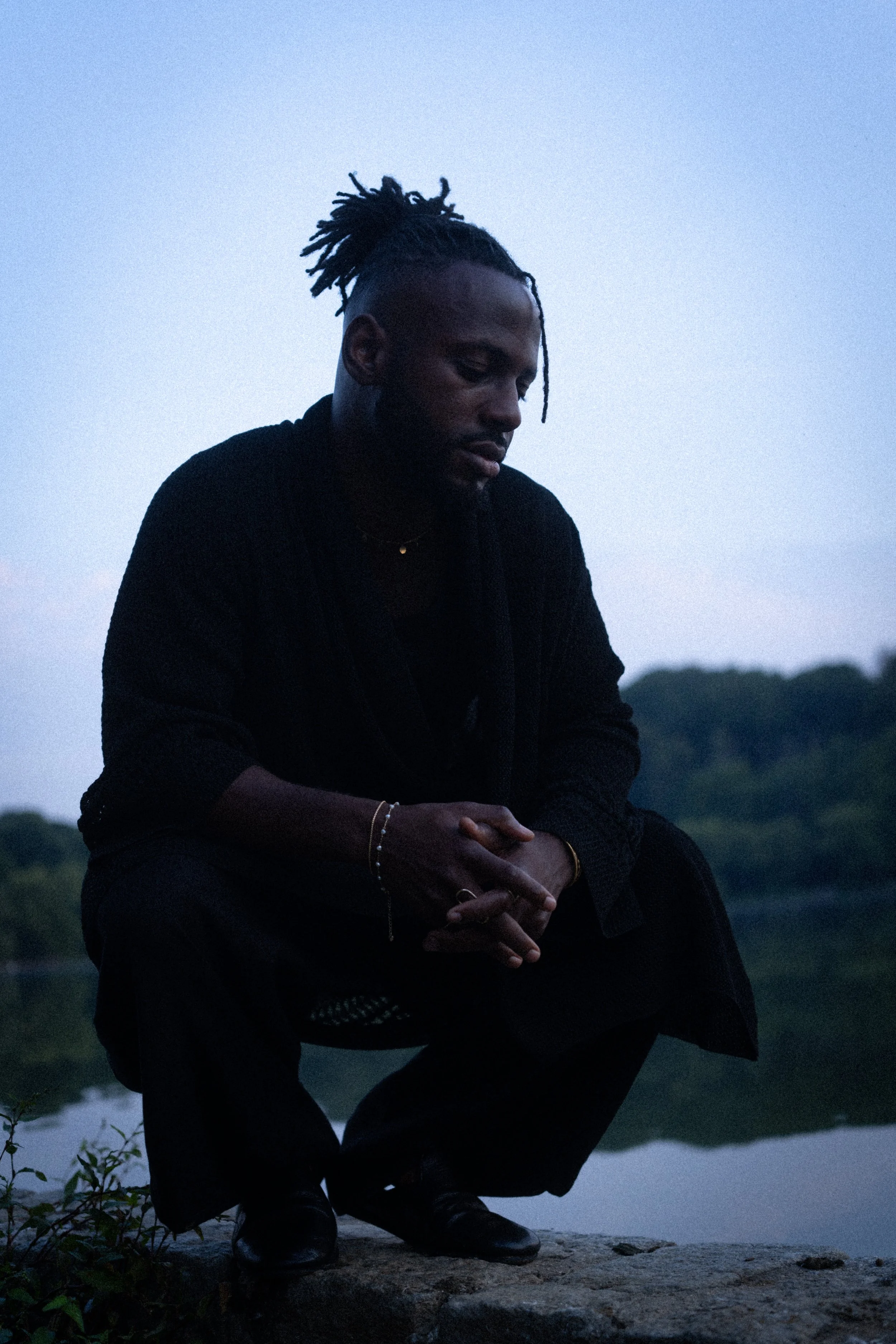 Brunson kneeling near a body of water during dusk or dawn, surrounded by trees.