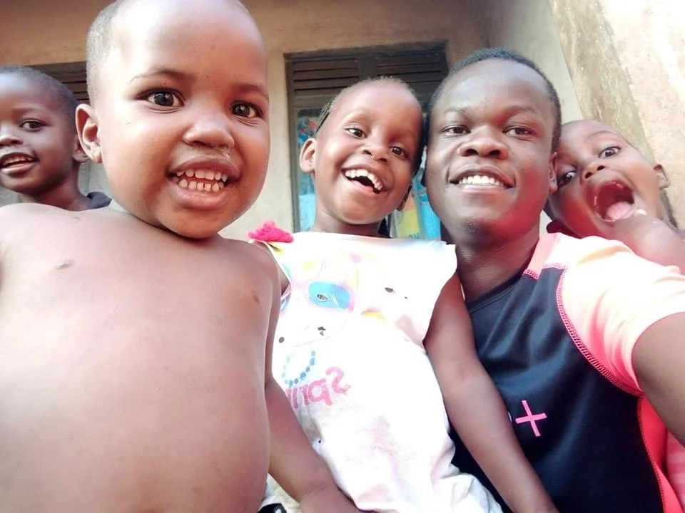Five smiling children and a young man taking a selfie outdoors in front of a house.