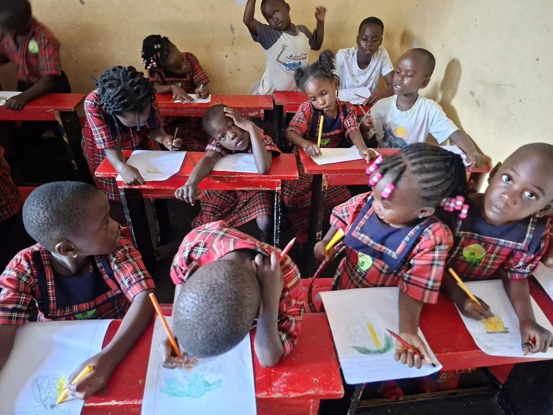 School children in uniforms drawing and coloring at desks in a classroom.