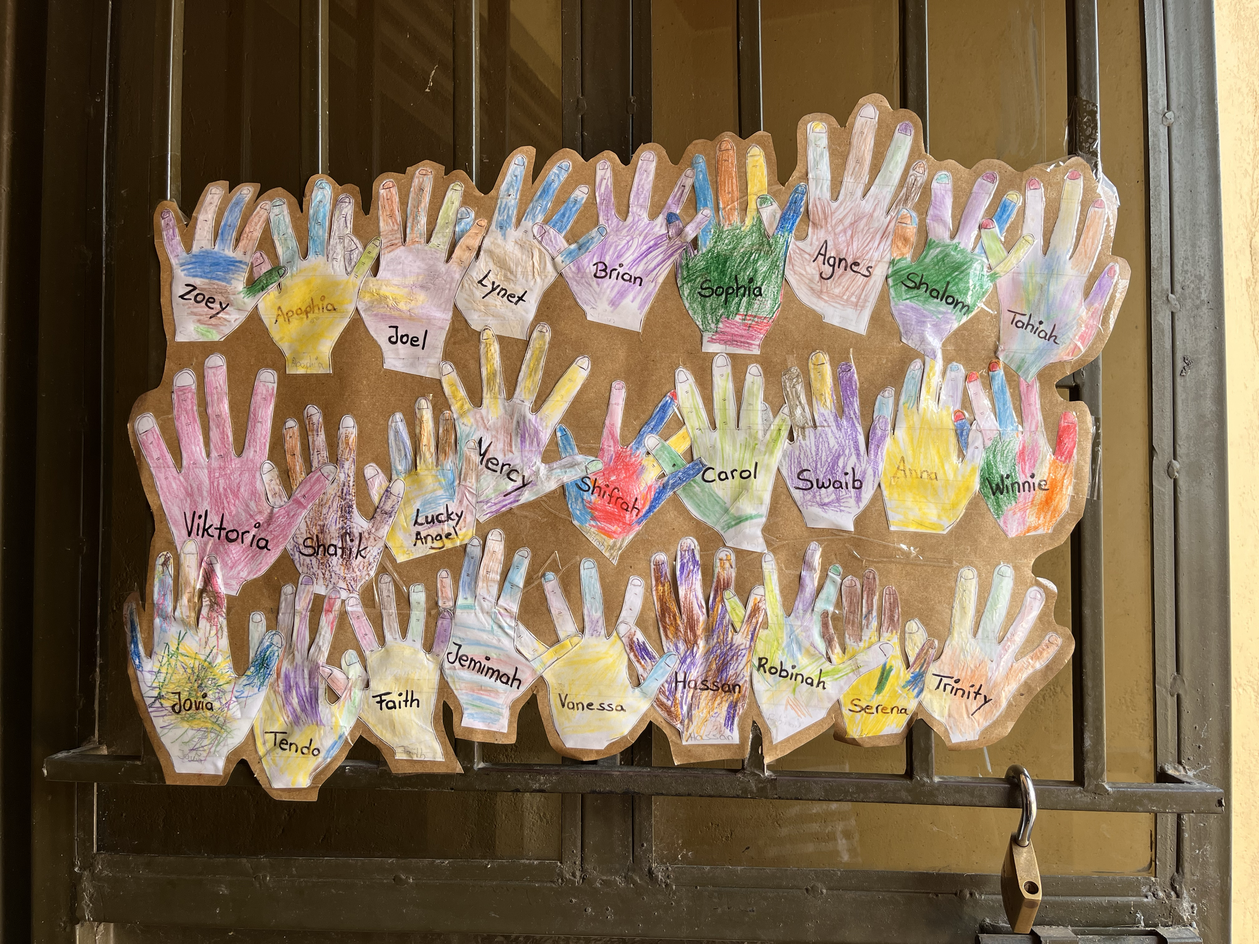Colorful paper cutouts of handprints with children's names written on each, decorated with colored pencils, displayed on a wooden background.