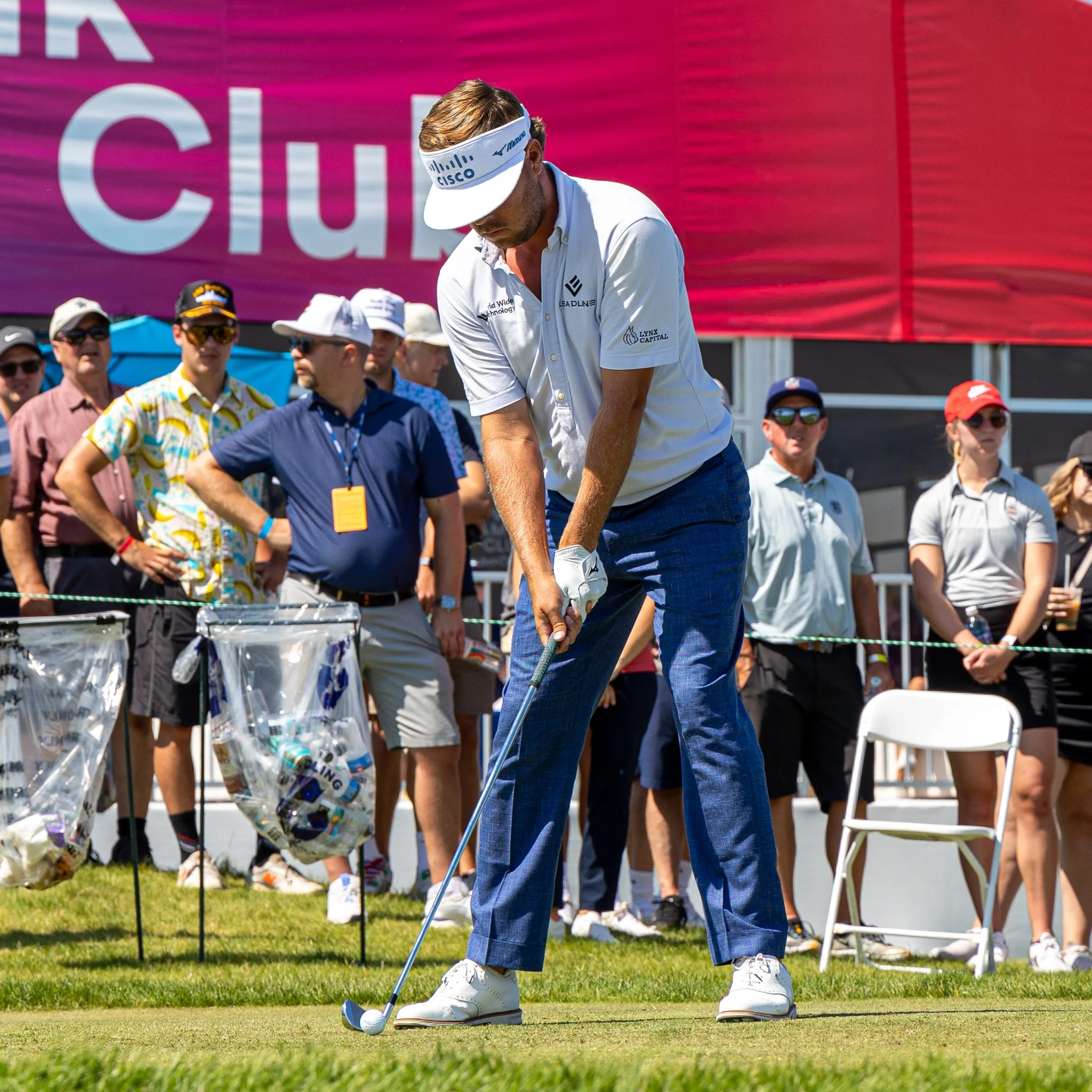 A man playing golf on a golf course, preparing to hit the ball while a group of spectators watch behind him.