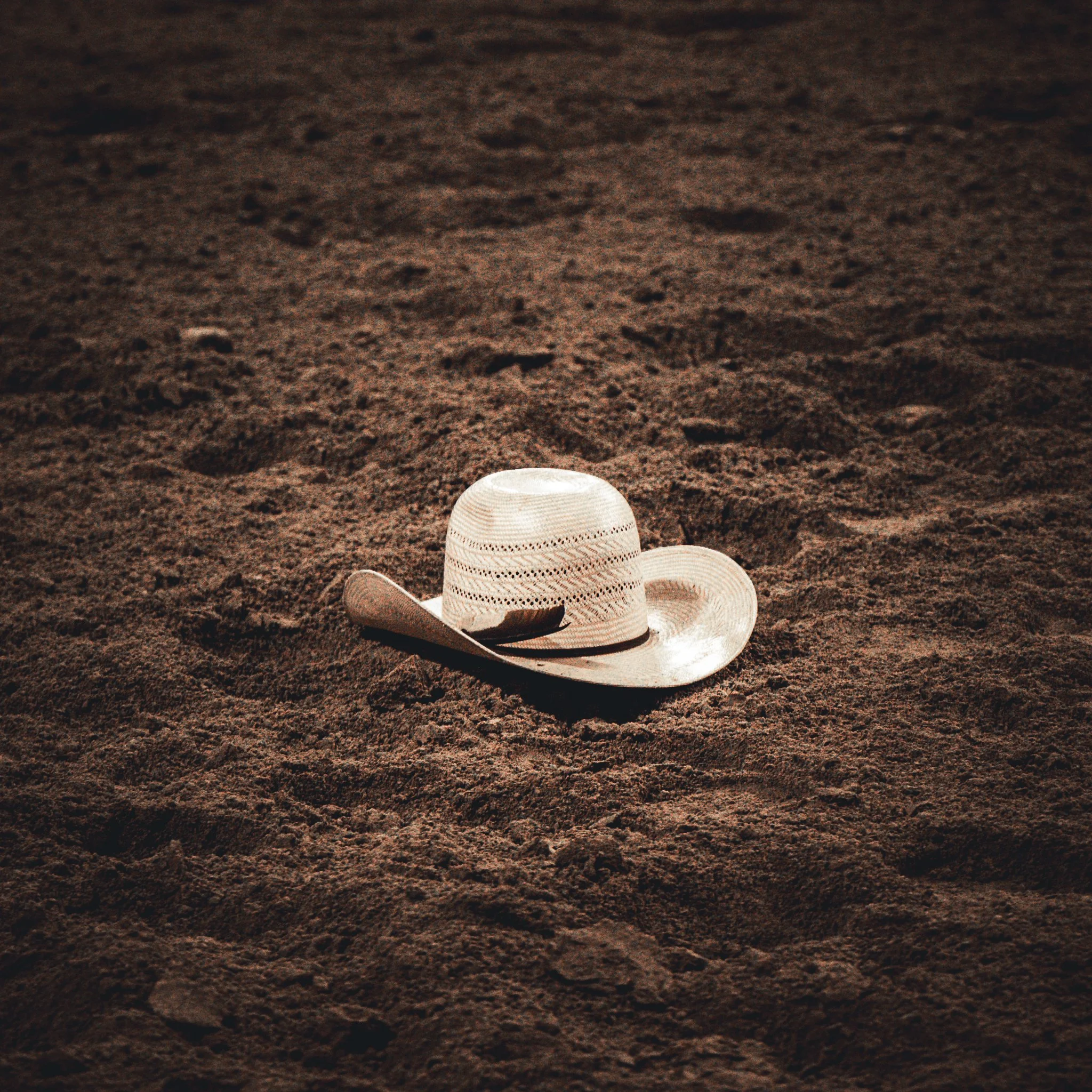 A cowboy hat lying on sandy ground.