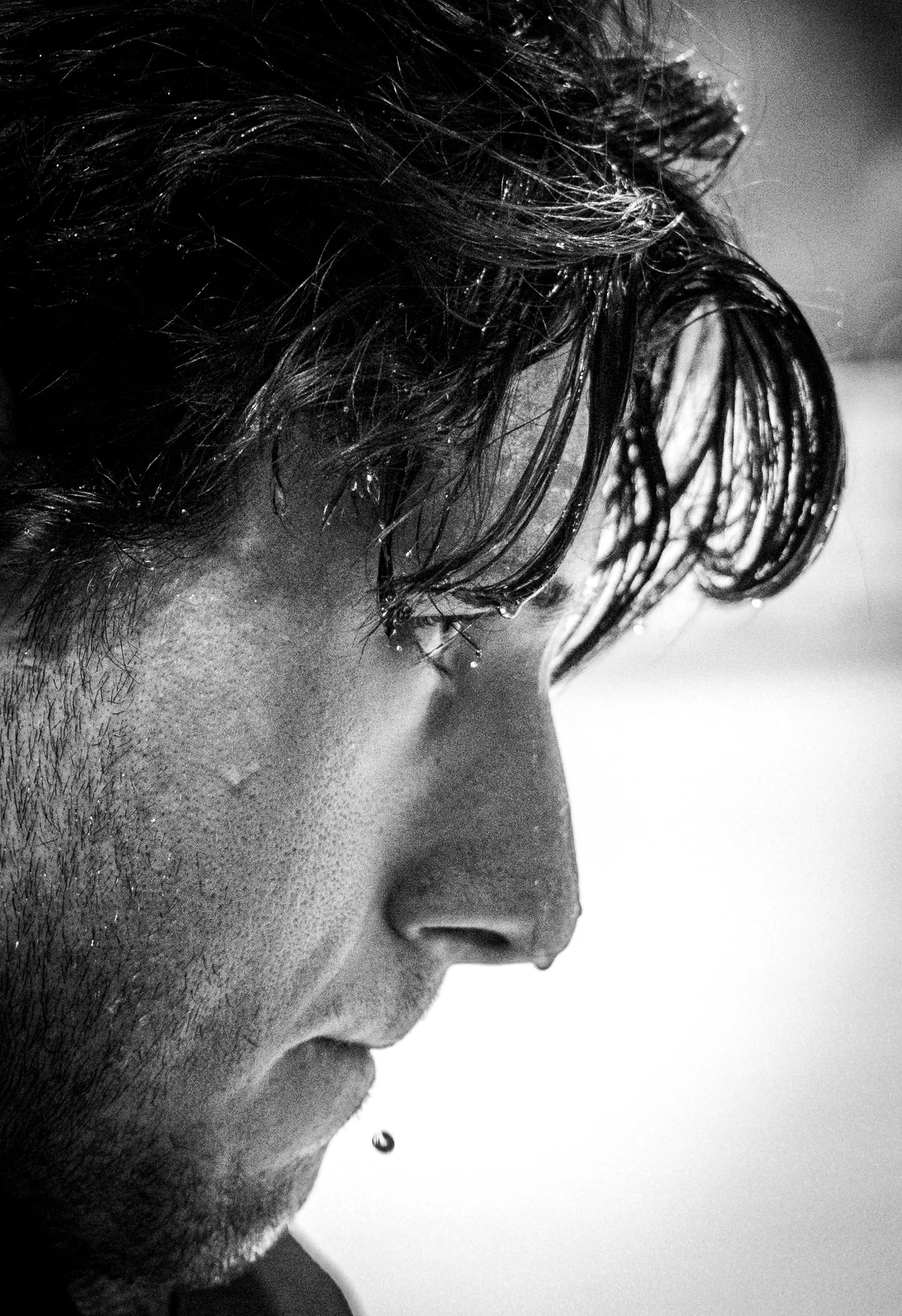 Close-up of a person's face in black and white, showing wet hair, with water droplets on their skin, and a water droplet falling from their nose.