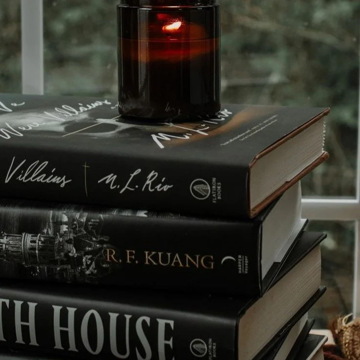 Instagram link; a stack of moody thrillers topped with a candle in a dark red glass.