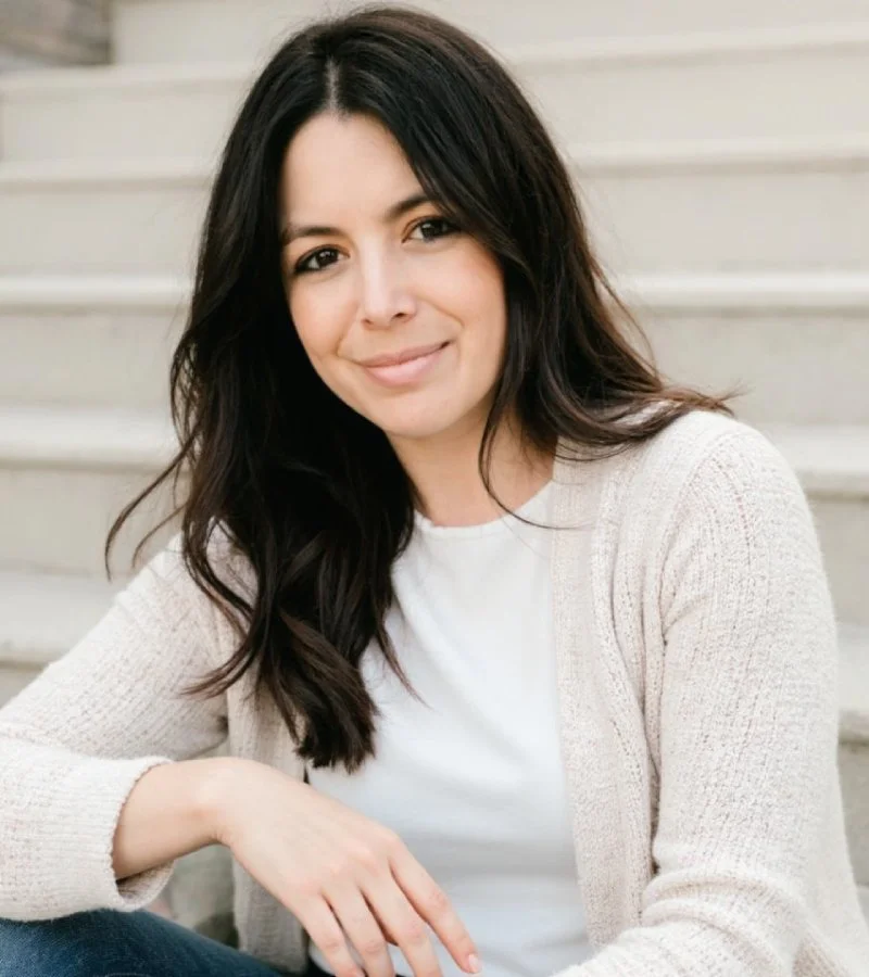 A woman with dark brown hair, dark brown eyes, and beige sweater, smiling.