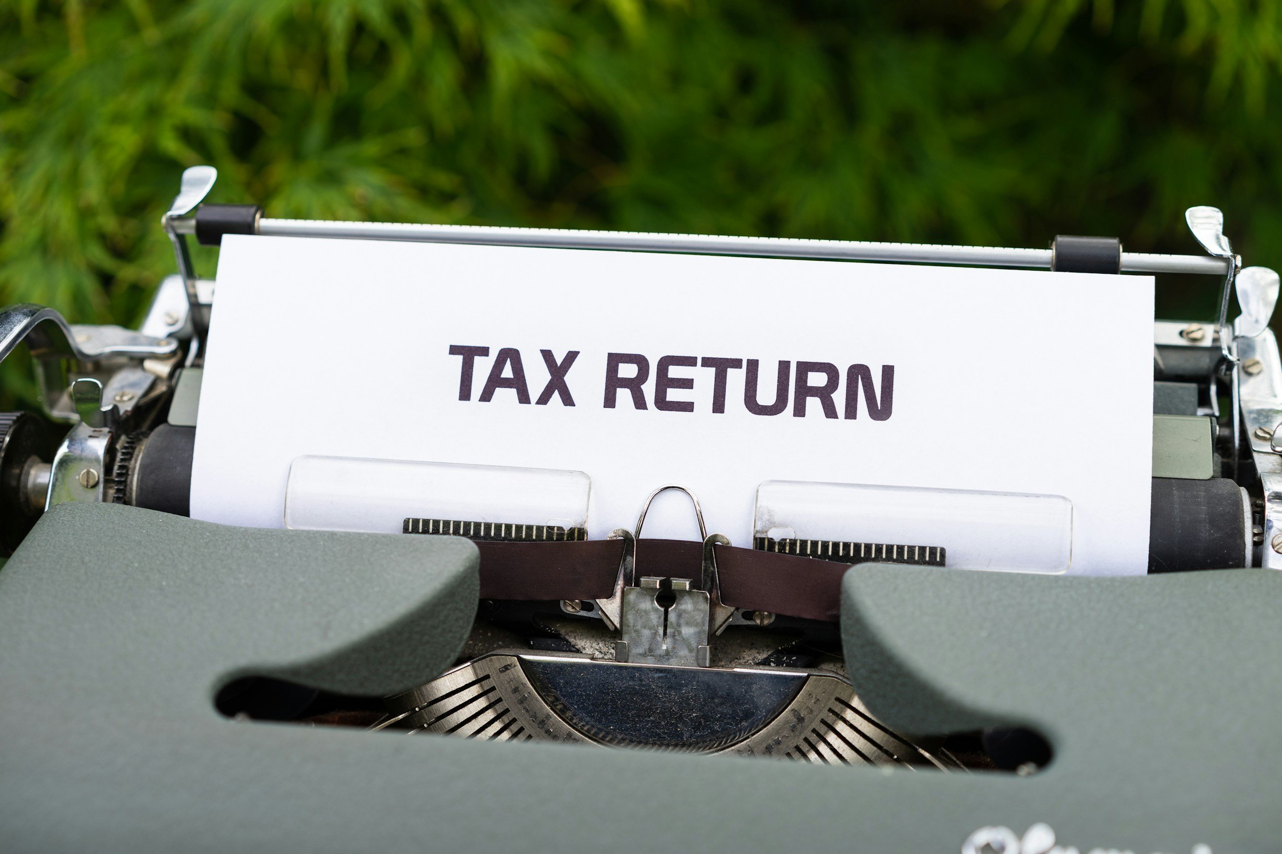 Typewriter with a paper displaying the text 'TAX RETURN' on a green surface.