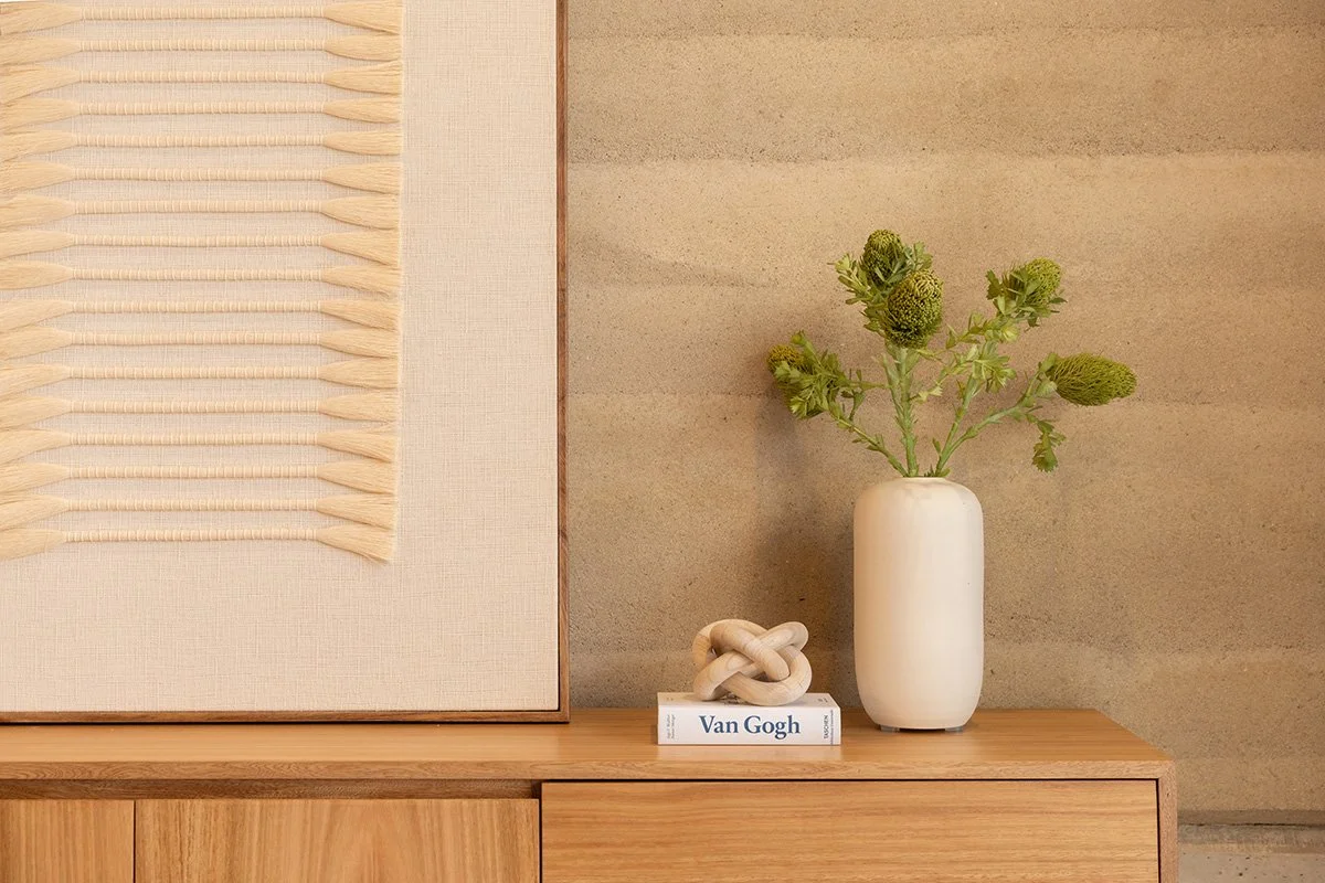 Decorative interior item with a white vase holding green flowers, a book titled "Van Gogh," and a geometric sculpture on a wooden surface against a beige wall.