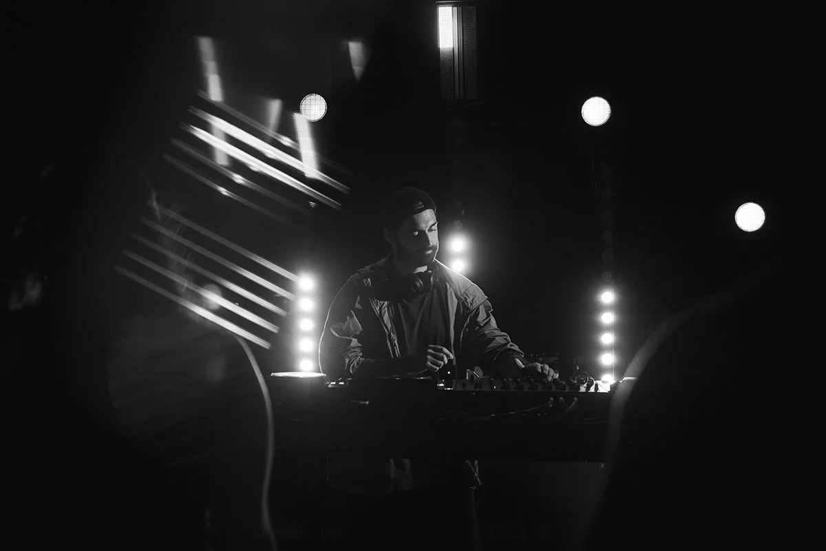 A DJ performing at a nightclub with lighting effects and silhouettes of the crowd in the foreground.