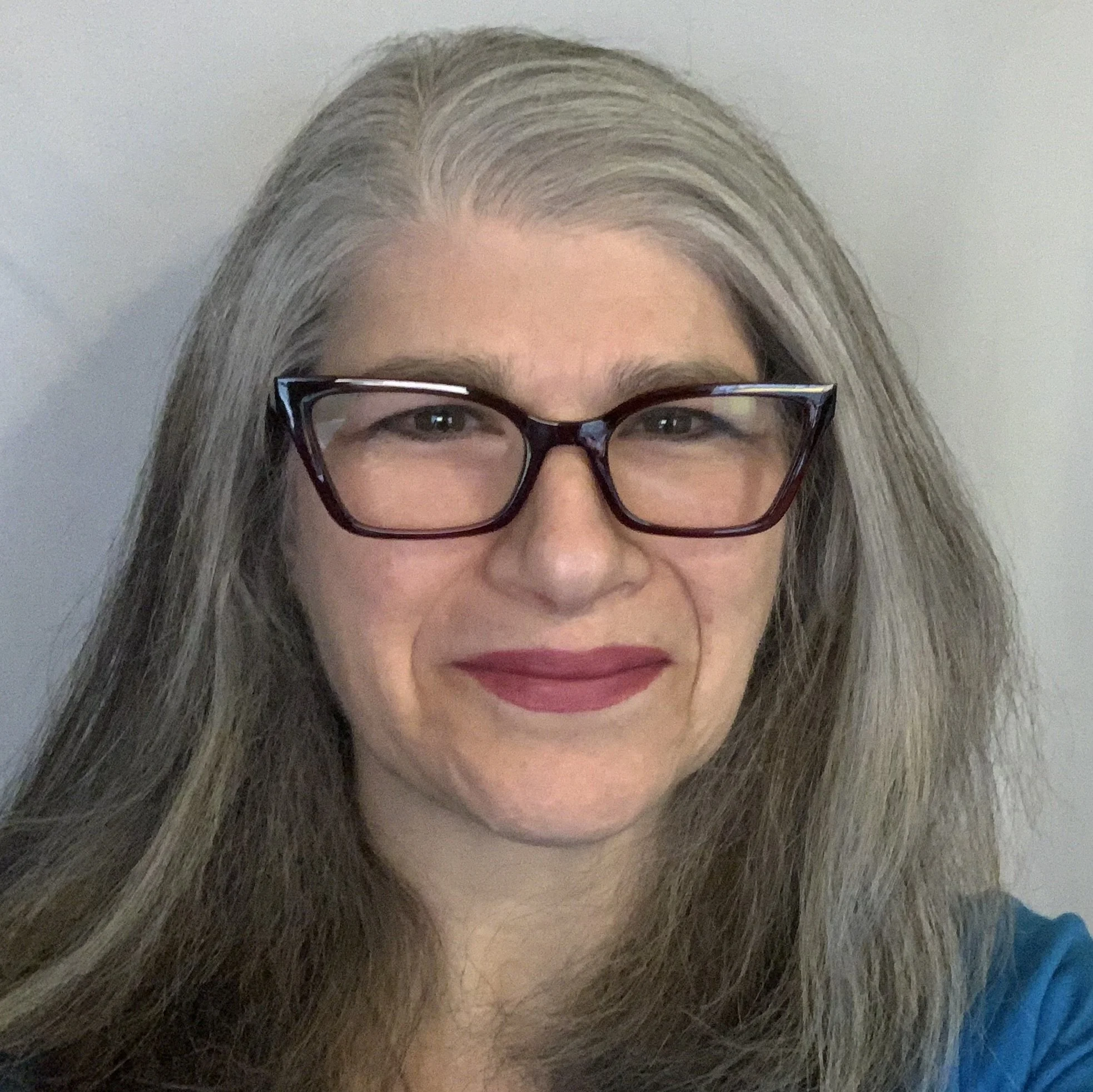 A woman with long gray hair and glasses, smiling at the camera.