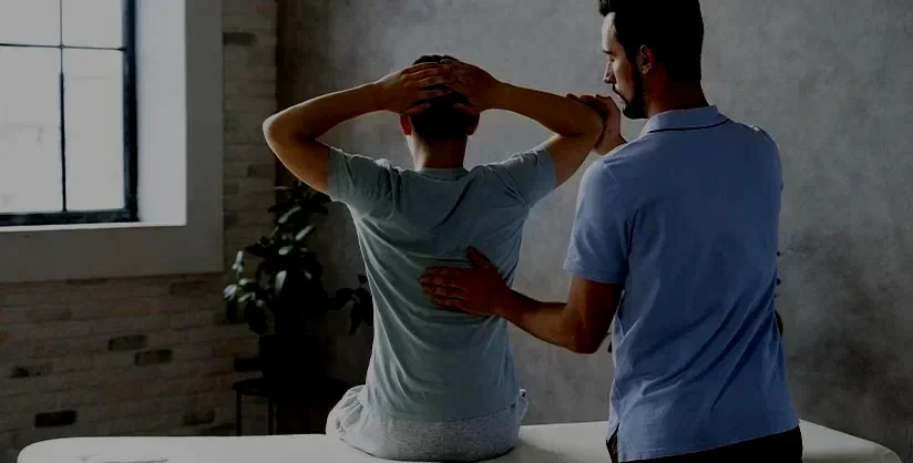 Un professionnel de santé examine un patient assis sur une table de clinique, dans une pièce lumineuse avec une fenêtre.