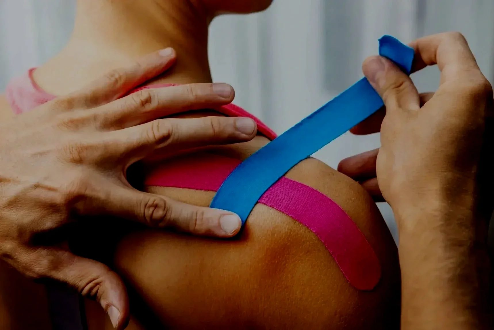 Une personne reçoit une thérapie de kinésithérapie avec des bandes bleu et rose sur l'épaule, sous la supervision d'un thérapeute.