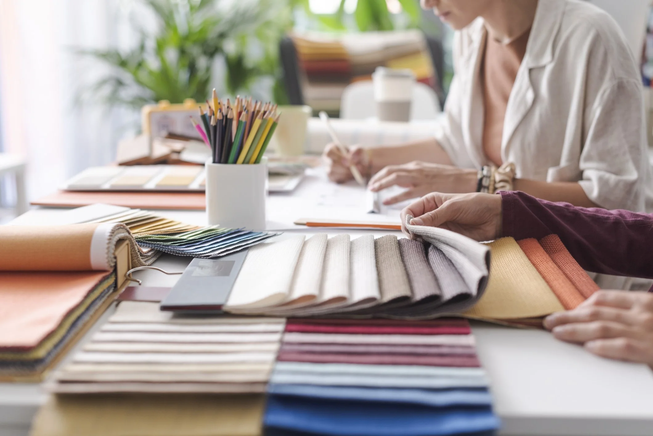 People working at a table with fabric swatches, color samples, and colored pencils for design or interior decorating.