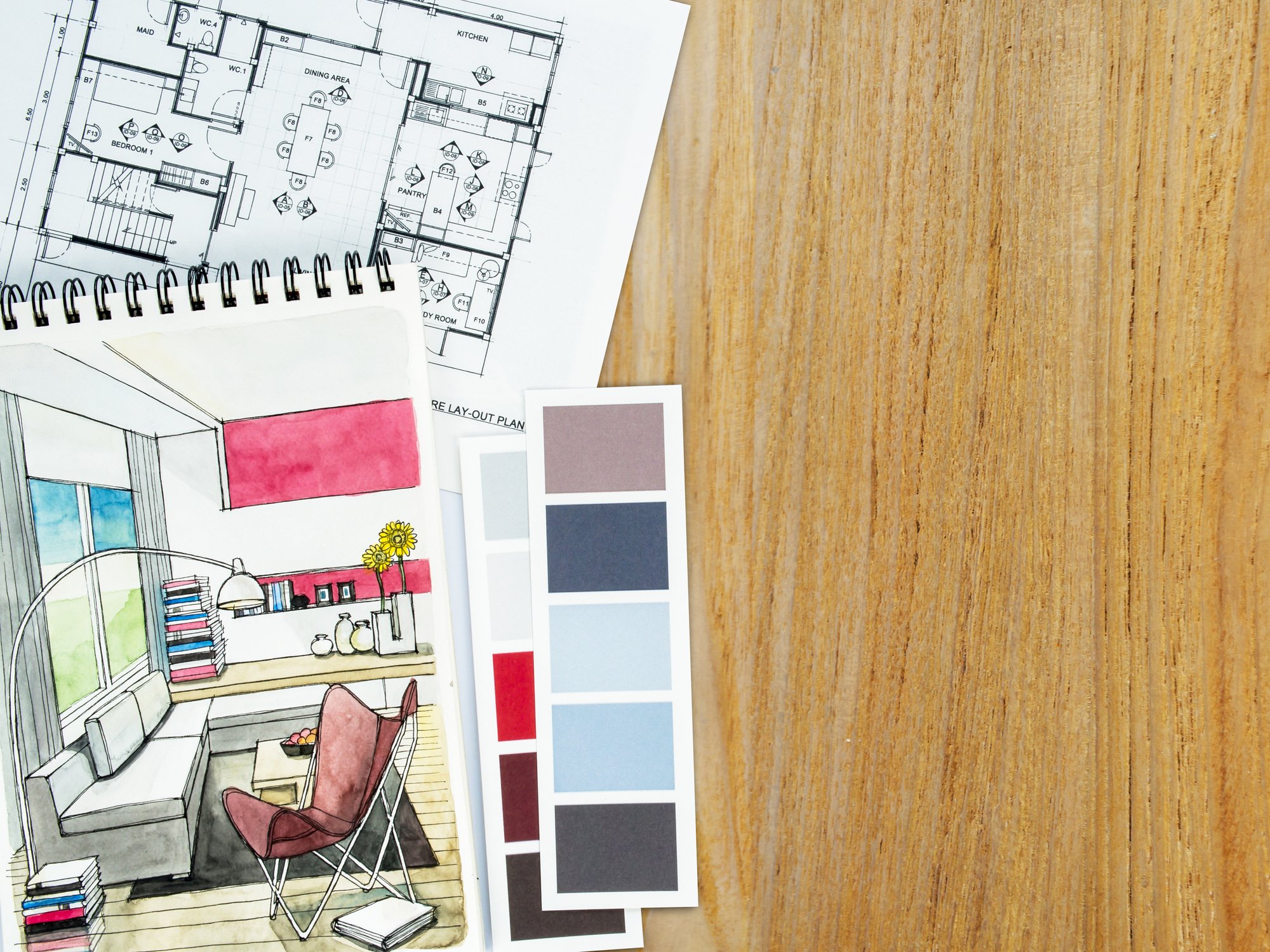Interior design mood board with hand-drawn sketches, technical blueprints, and fabric and paint swatches laid on a wooden surface