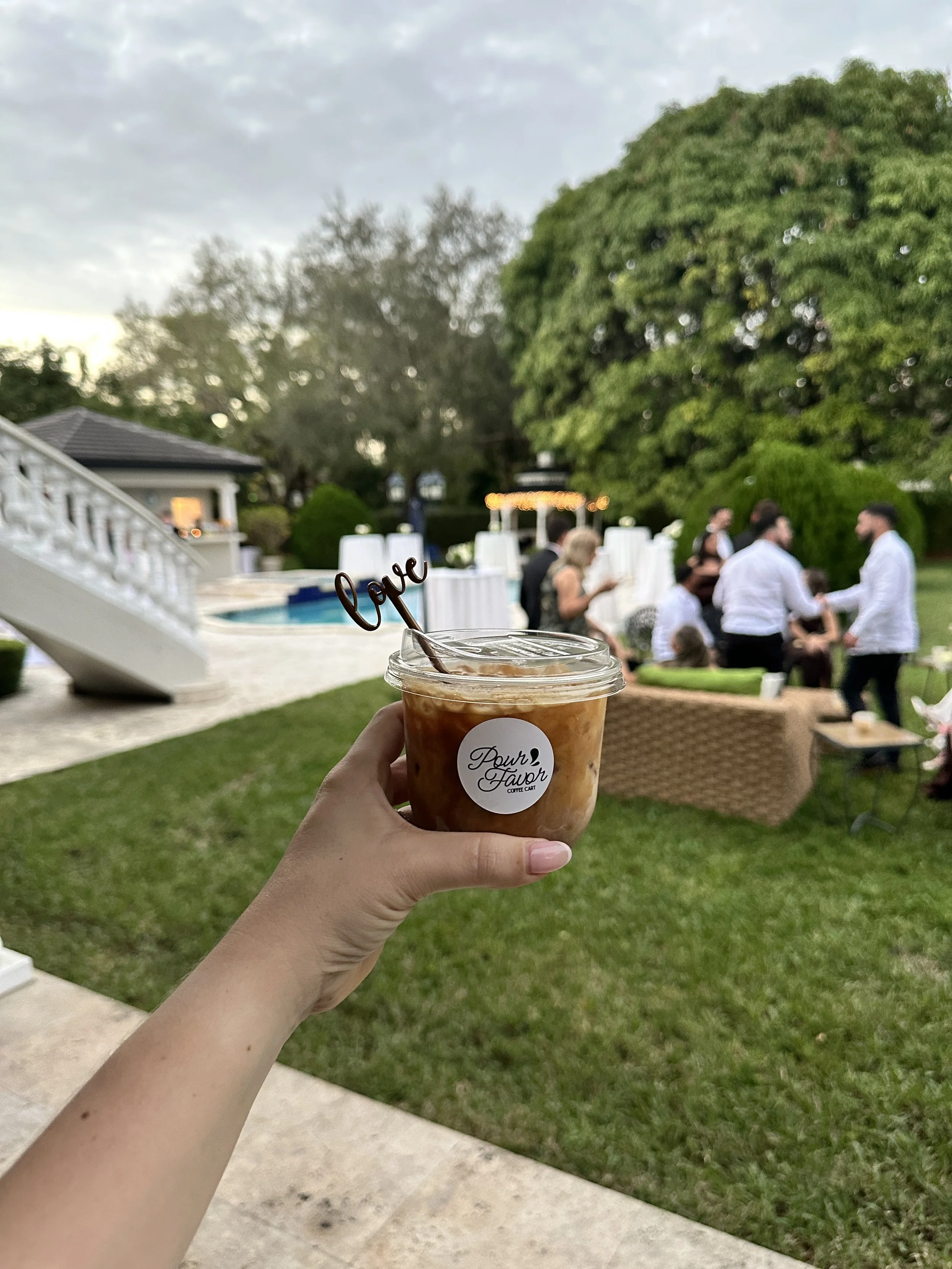 Iced coffee from a Miami wedding coffee bar during an outdoor cocktail hour with guests in the background