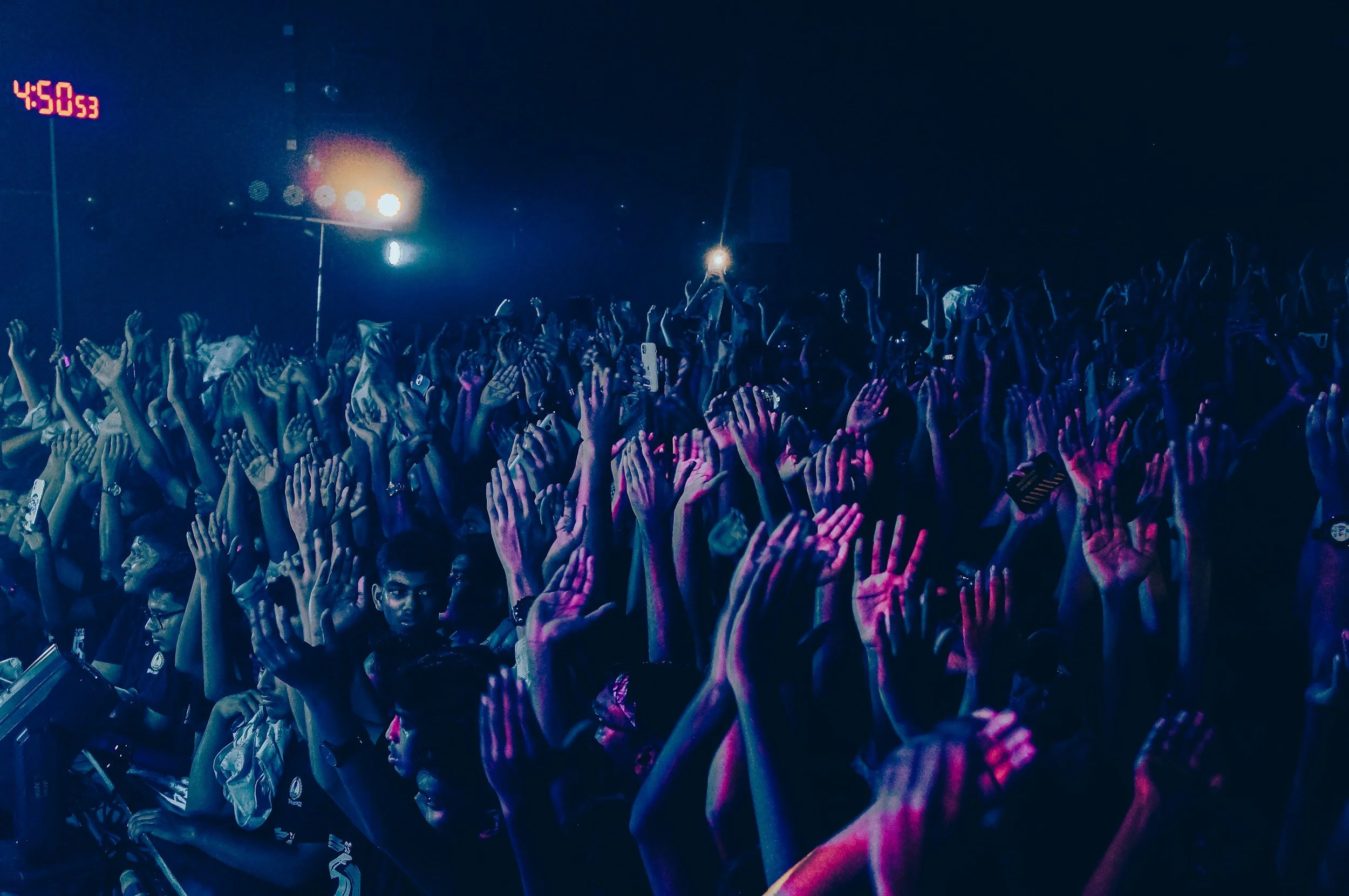 People at a concert concert with hands raised, illuminated by colorful lights