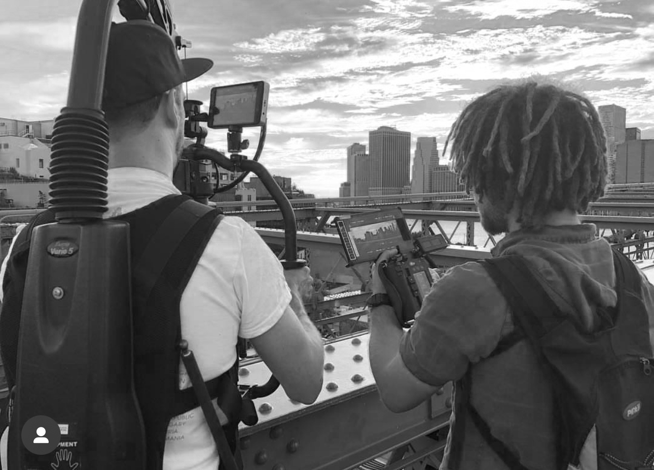 Two videographers filming a cityscape with tall buildings and a sky filled with clouds.