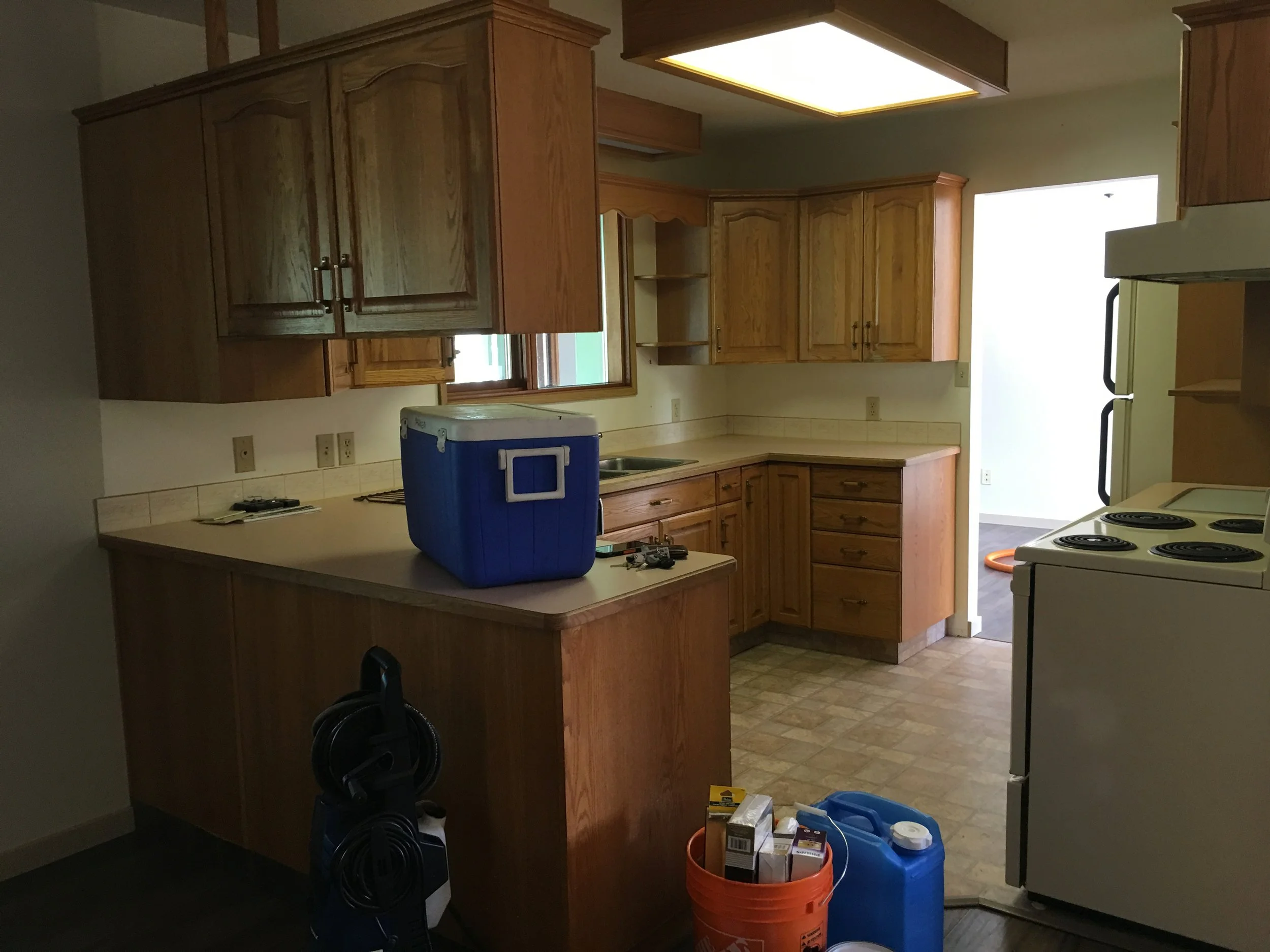 Dark outdated 80's kitchen with orange oak cabinetry and almond coloured appliances.