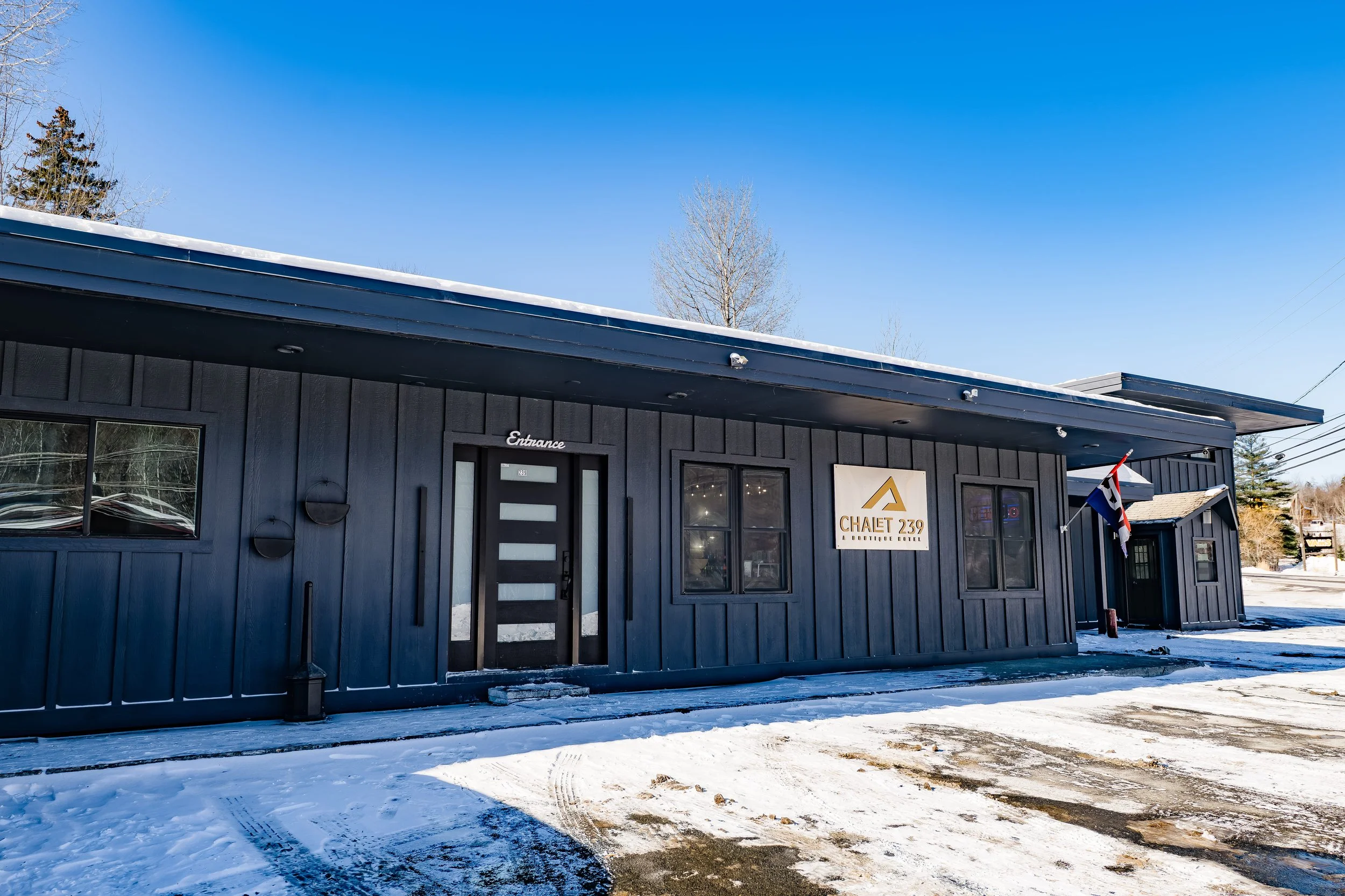 Exterior view of Chalet 239, a boutique hotel with black wooden siding, snow-covered ground, and a clear blue sky.