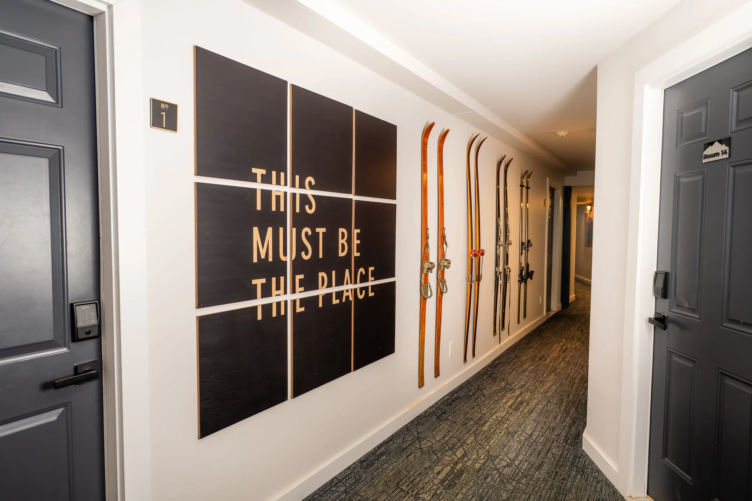 Hallway with a black sign that reads "This Must Be The Place" and vintage skis mounted on the wall.