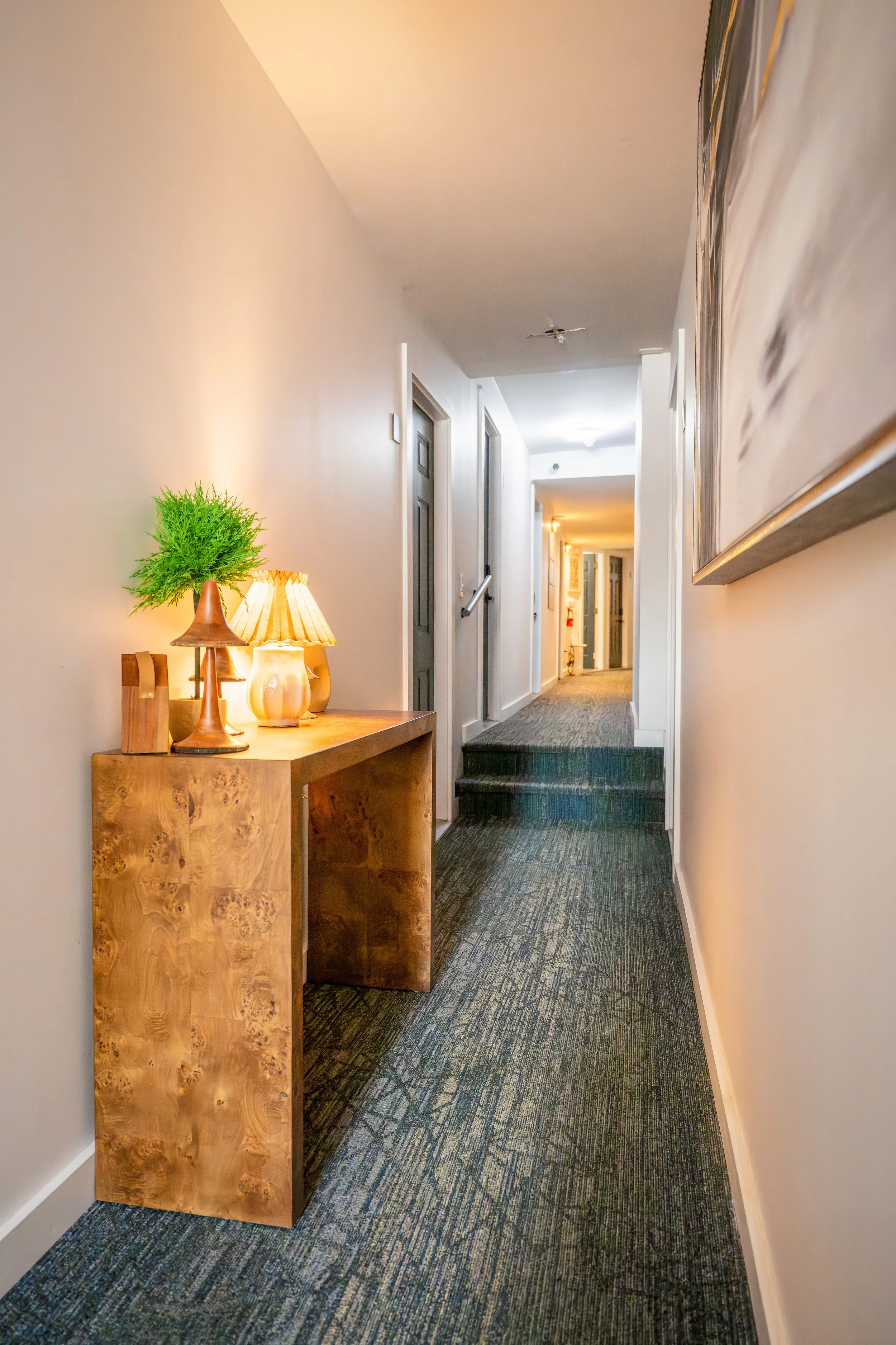 Hotel hallway with a wooden console table, lamps, and artwork along the walls.