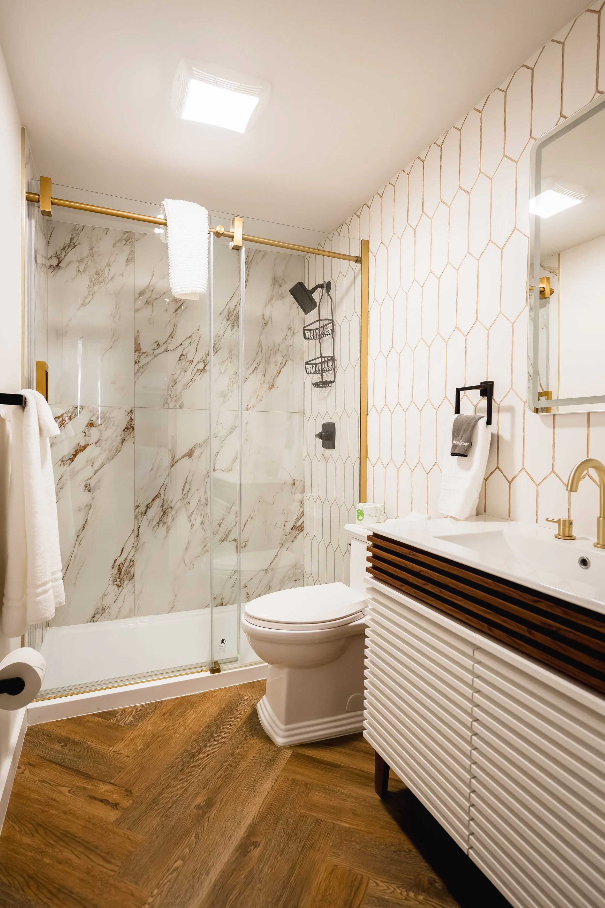Modern bathroom featuring a walk-in shower with marble walls, a white toilet, a vanity with a white and wood design, and a mirror with a white frame.