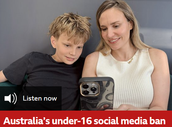 A woman and a young boy are sitting on a couch, looking at a smartphone together and smiling.