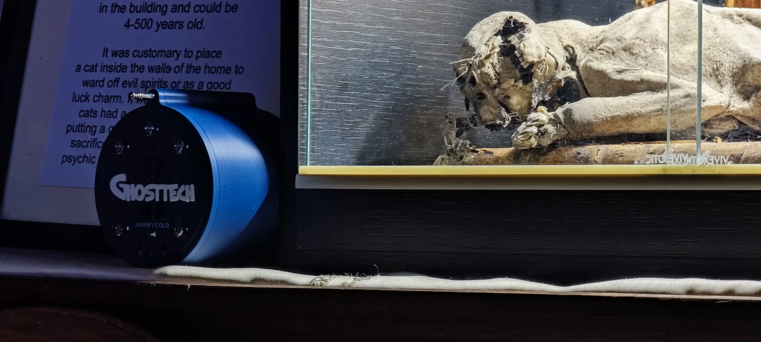 A skeleton of a small animal, possibly a rodent, inside a glass display case, next to a blue GhostTech device and a partially visible sign with instructions or information.