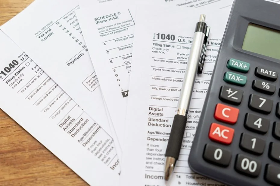 Multiple forms of US tax documents, a calculator, and a pen on a wooden surface.