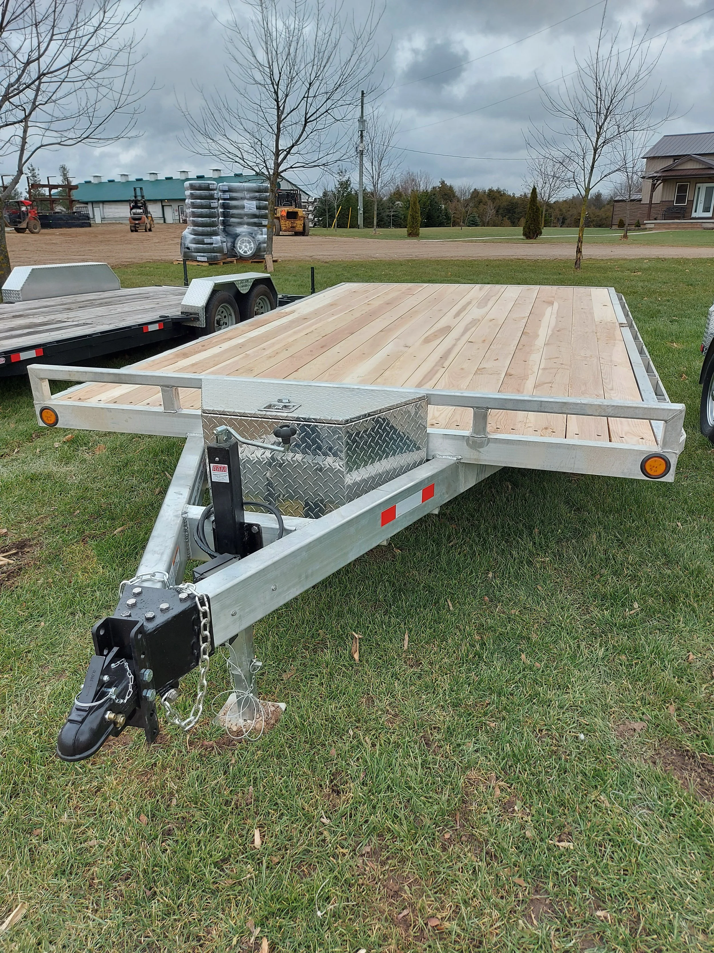 An empty flatbed utility trailer with a wooden deck and metal sides, parked on grass in an outdoor area.