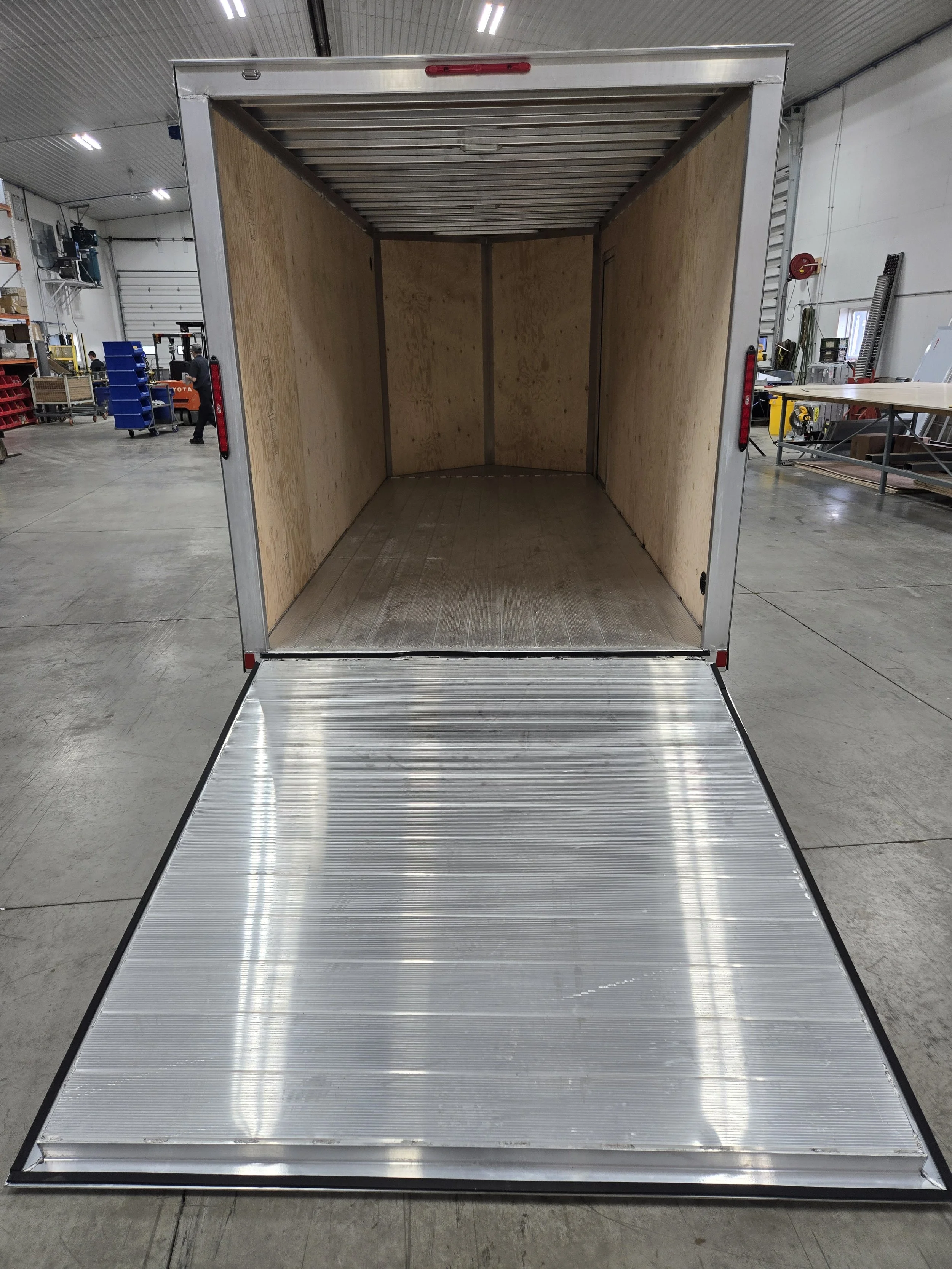 Empty cargo trailer with open ramp door inside a warehouse.
