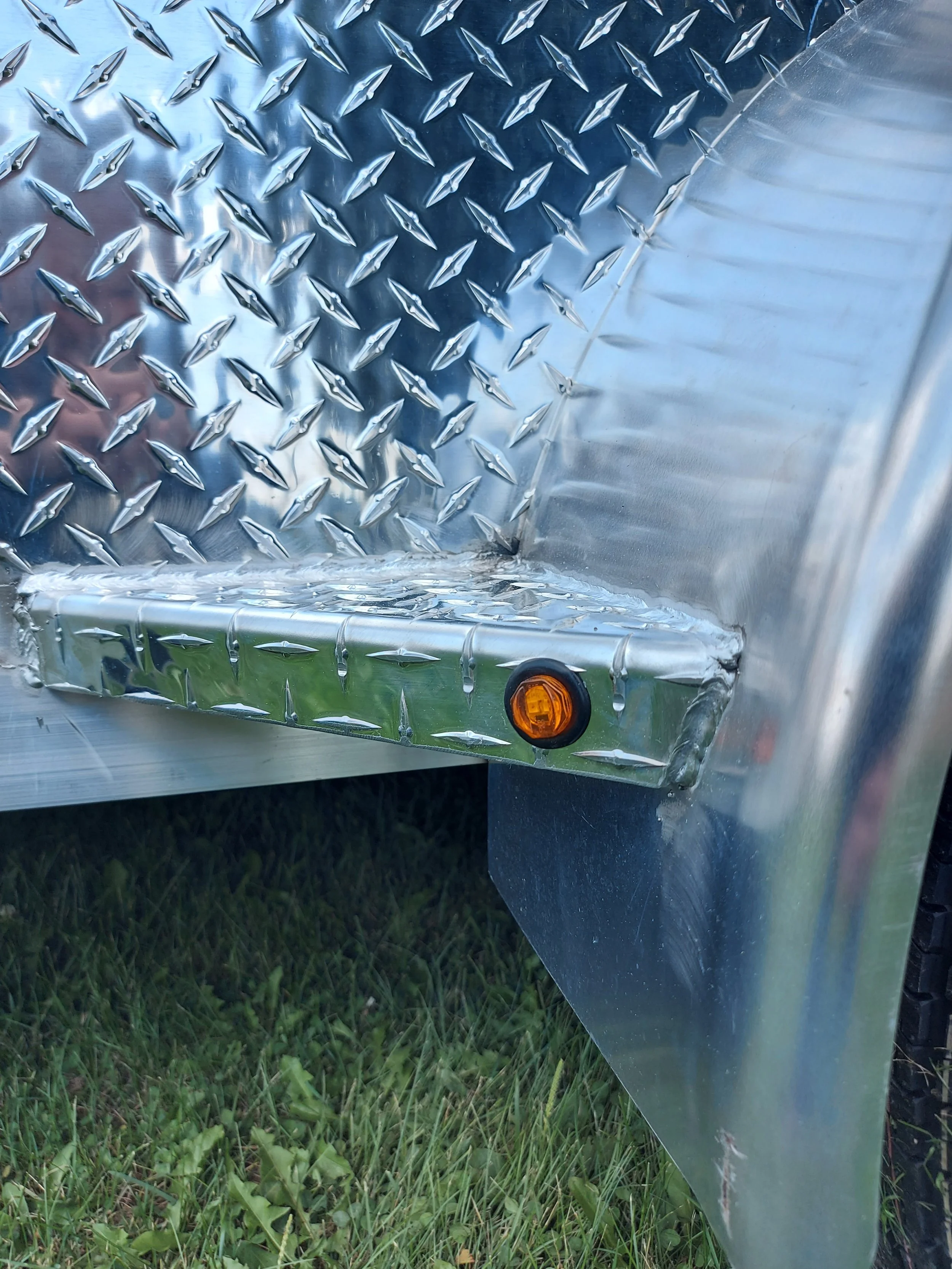 Close-up of a metallic diamond plate surface on a trailer, with a small amber reflector light near the bottom edge.