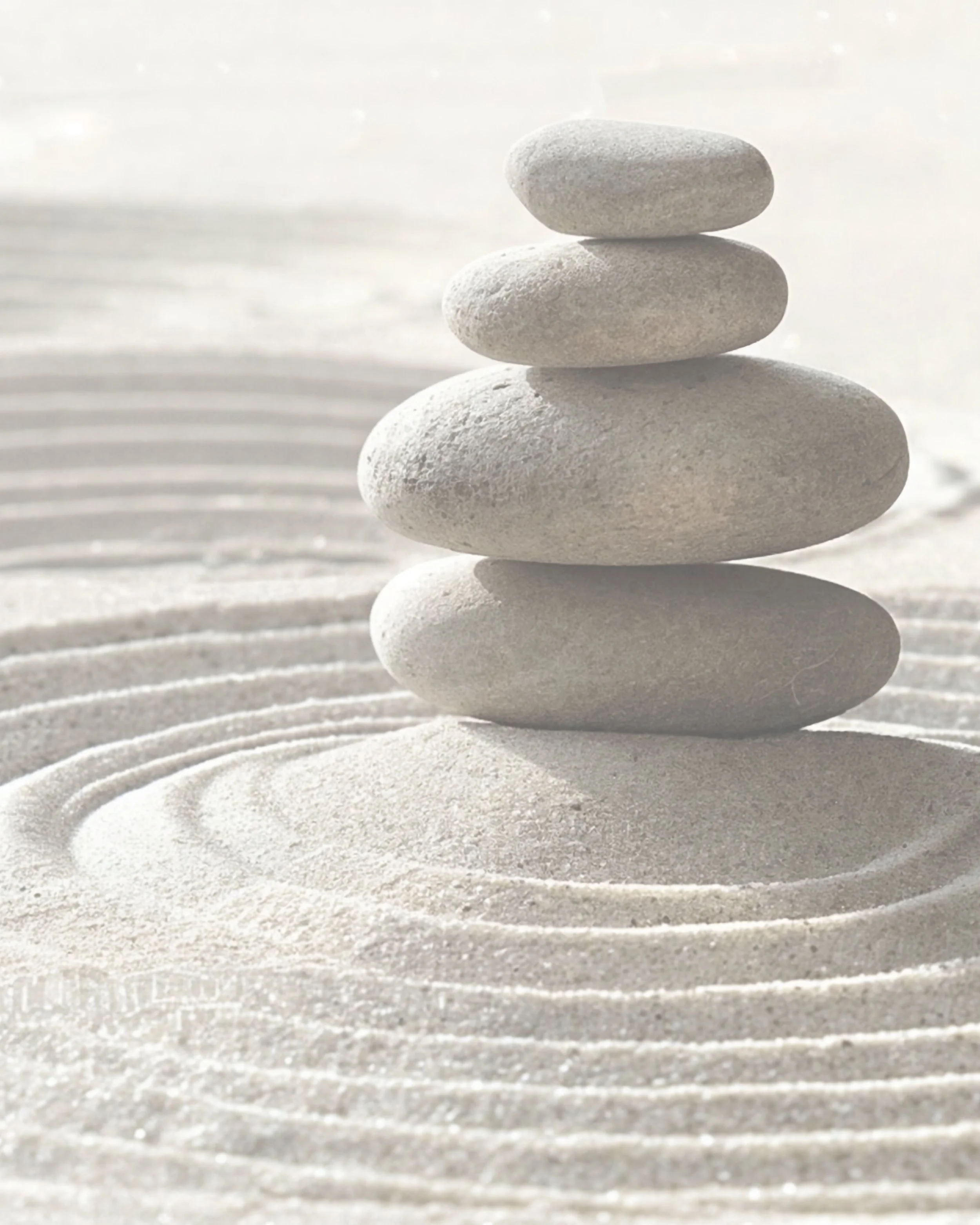 A stack of five smooth, rounded stones balanced on top of each other on white sand with circular raked patterns.