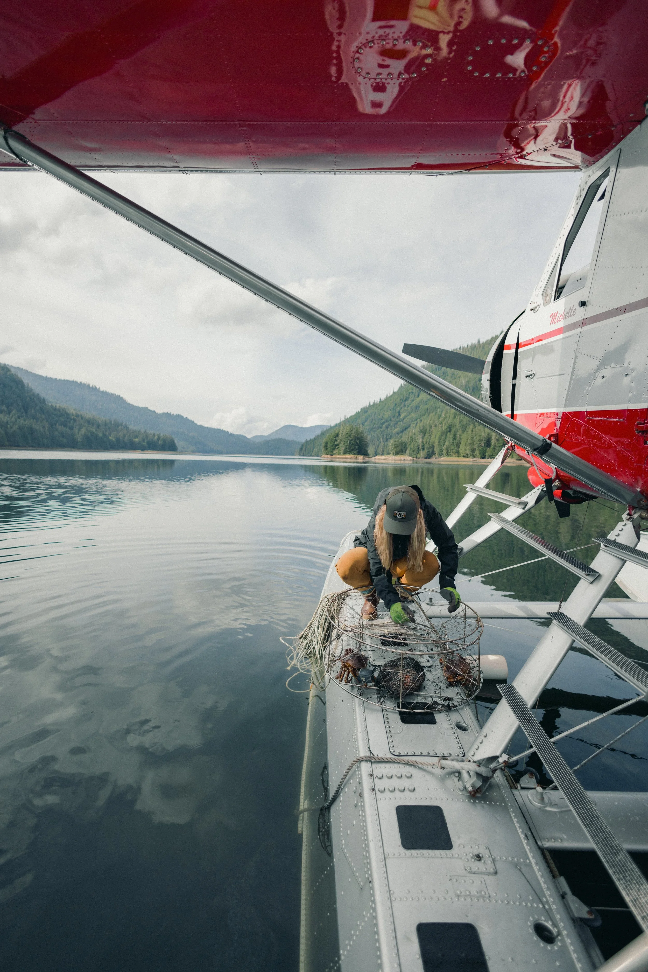 A person on a seaplane retrieving lobsters from a trap in a calm lake surrounded by green mountains.