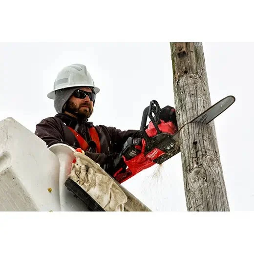 A utility worker in safety gear using a chainsaw to cut down a wooden utility pole from an elevated bucket lift.