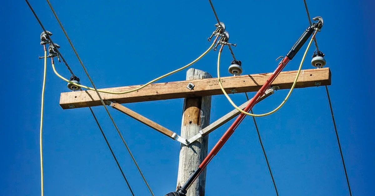 Close-up of a wooden utility pole with electrical insulators and wires against a clear blue sky.