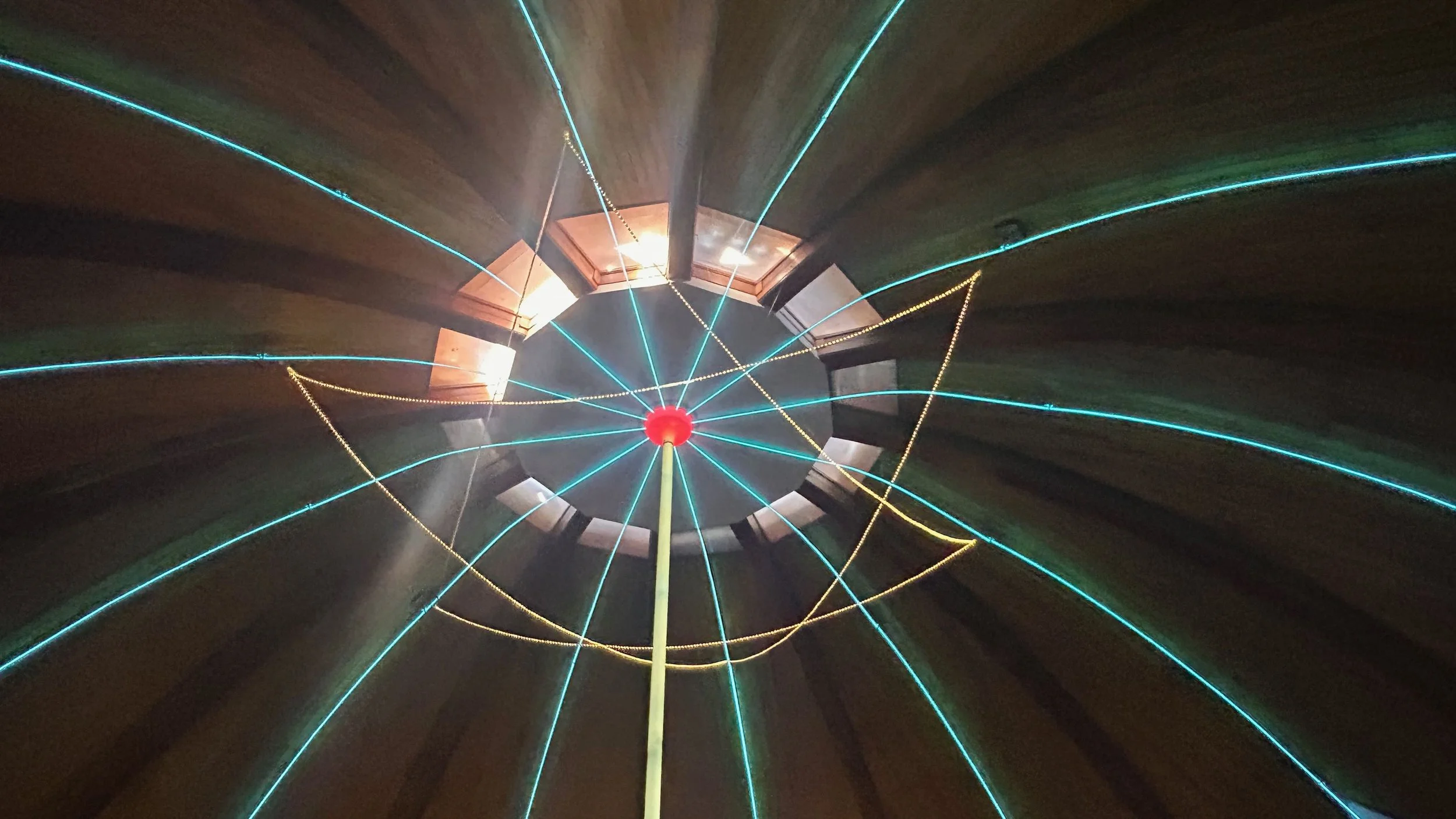 Looking up inside a tall, wooden amusement park ride with bright blue and yellow lights radiating outwards from a central point at the top.