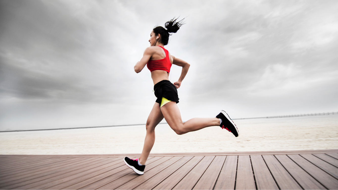 A woman jogging on a wooden path near a body of water on a cloudy day
