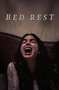 A woman with long dark hair screaming or yelling in a bedroom with the words 'BED REST' on the wall behind her.