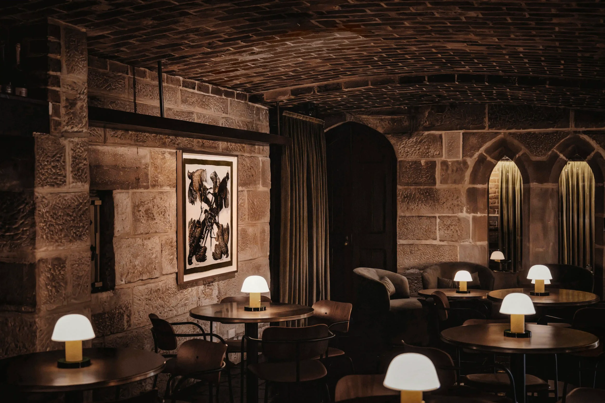 A woman with dark hair in a sleeveless black dress and a smiling man in a white chef's coat standing together in a warmly lit restaurant or kitchen setting.
