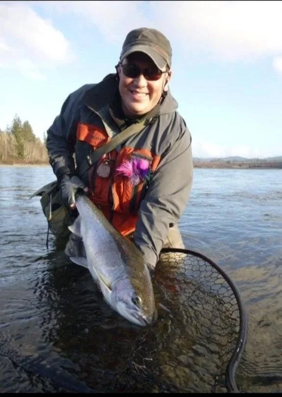 Person in outdoor fishing gear holding a large fish over water, with a fishing net in the foreground.