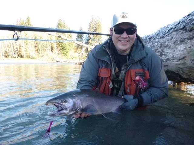 Person in outdoor gear holding a large fish in a river with trees in the background.