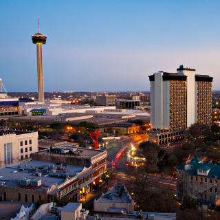 Nighttime cityscape featuring the Stratosphere Tower with a lit observation deck, surrounded by tall buildings and city lights in Las Vegas.