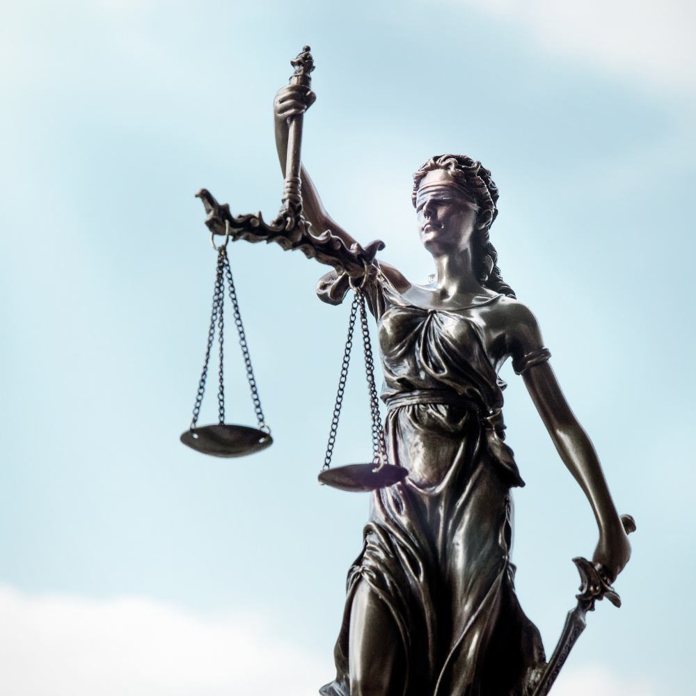 Statue of Lady Justice holding a sword and scales against a cloudy sky.