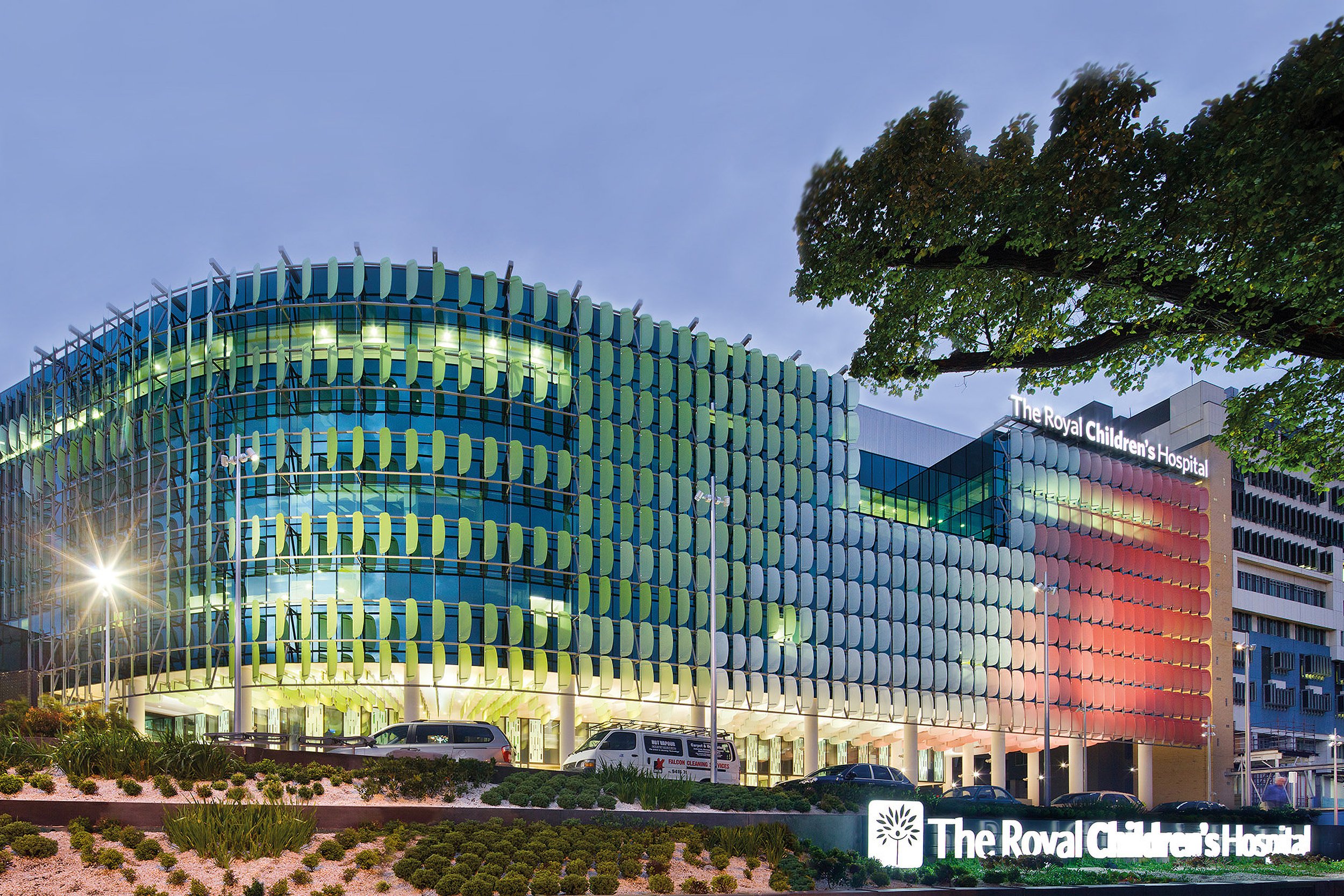 The Royal Children's Hospital building illuminated at dusk with colorful exterior lighting and a landscaped area in the foreground.